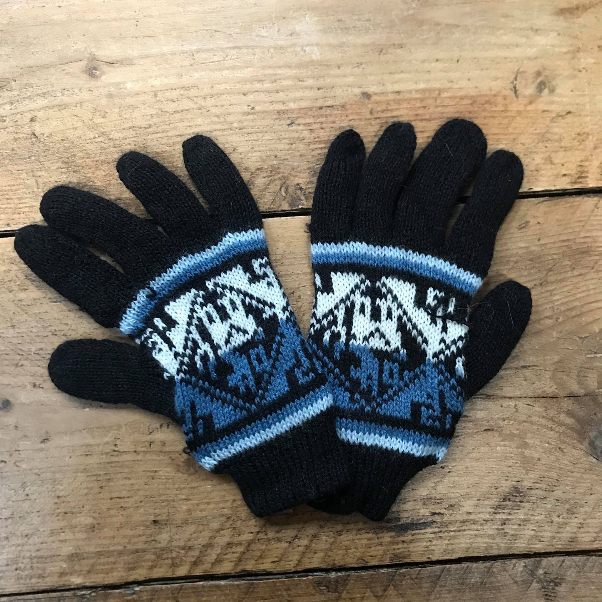 A pair of blue knitted gloves with geometric patterns on a white wooden surface.