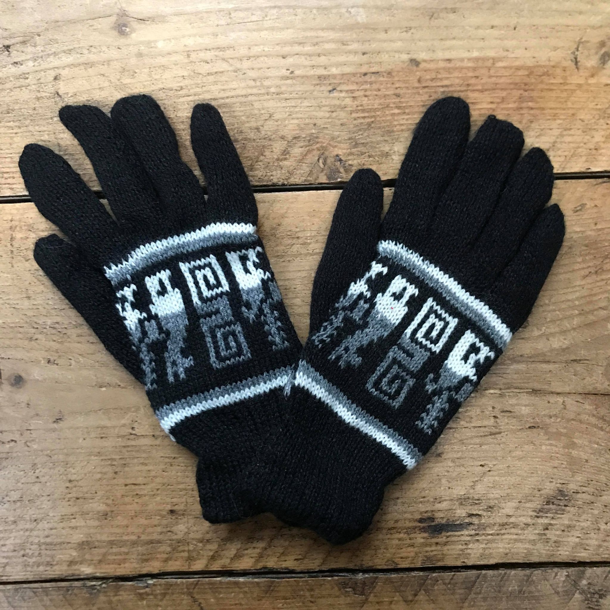 A pair of blue knitted gloves with geometric patterns on a white wooden surface.
