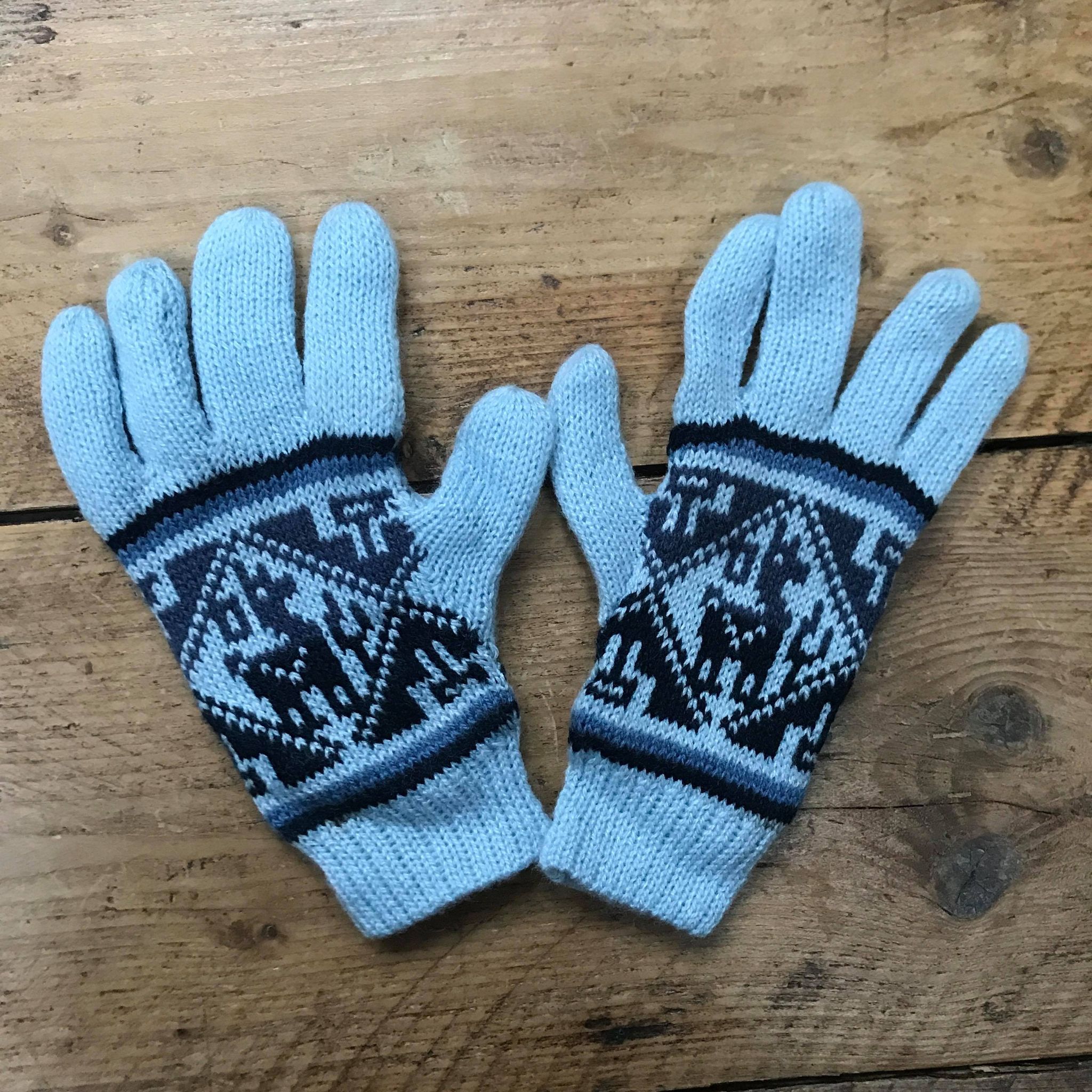 A pair of blue knitted gloves with geometric patterns on a white wooden surface.