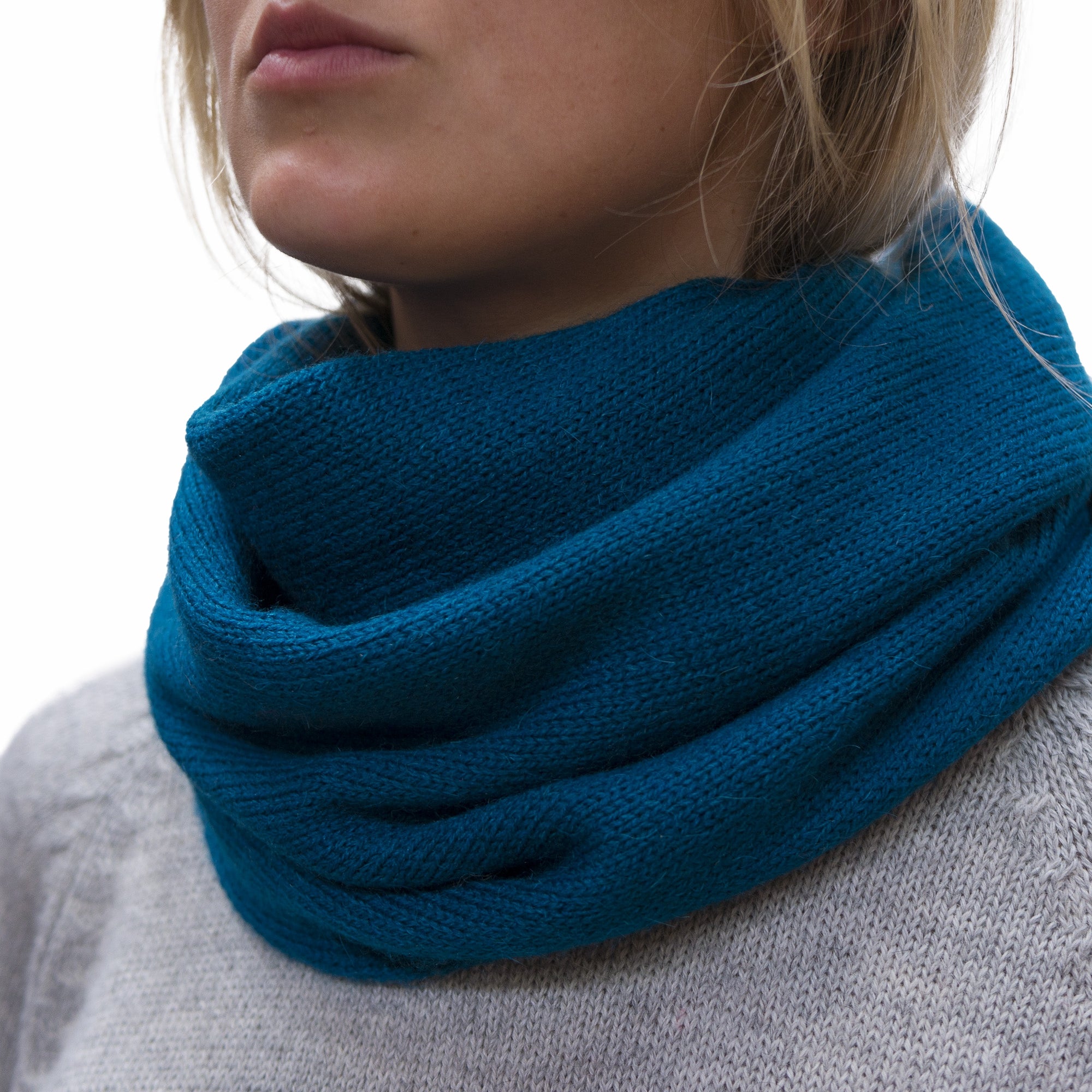 A person wearing a teal blue alpaca blend tube scarf wrapped around the neck.